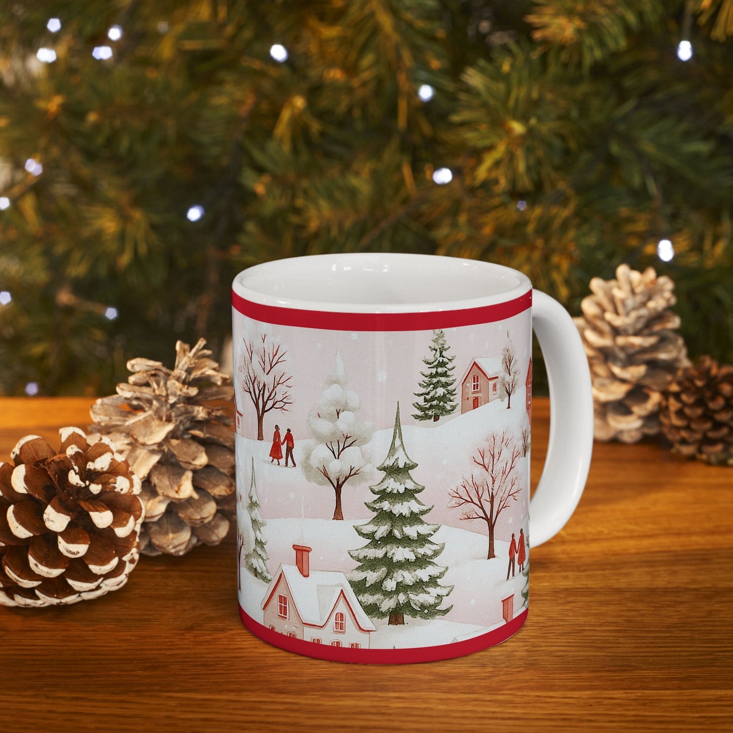 Christmas mug with snowy village and pine trees design, placed on wooden table with pinecones and festive tree lights in the background