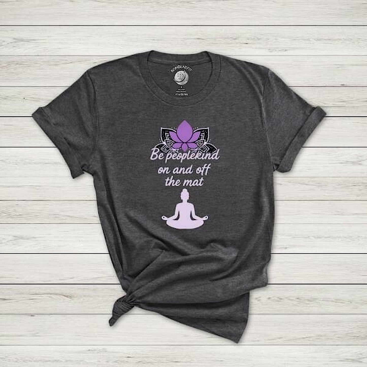 Dark Grey Heather Bella Canvas 3001 t-shirt with lotus and "Be peoplekind on and off the mat" quote, flat lay on wood.