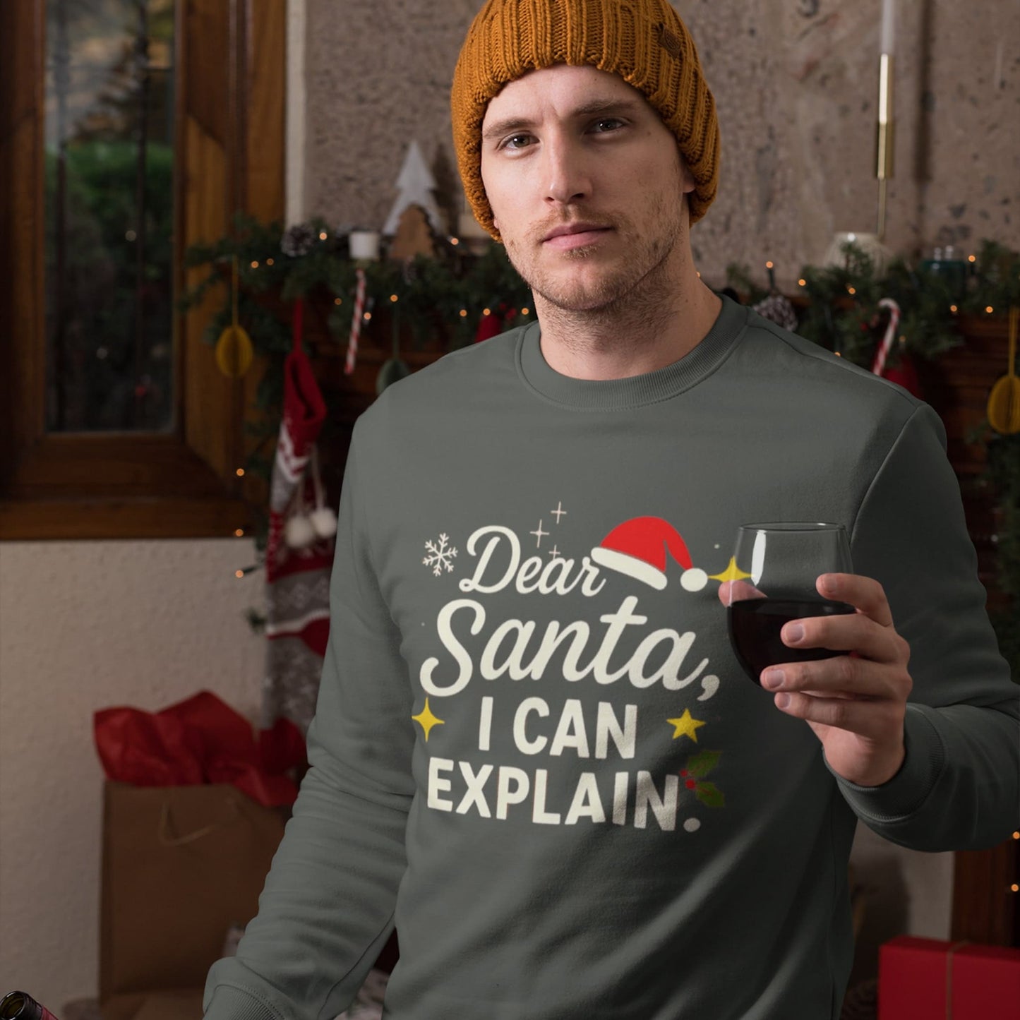 Man in green “Dear Santa, I Can Explain” sweatshirt holding wine glass in cozy Christmas setting with festive decorations.