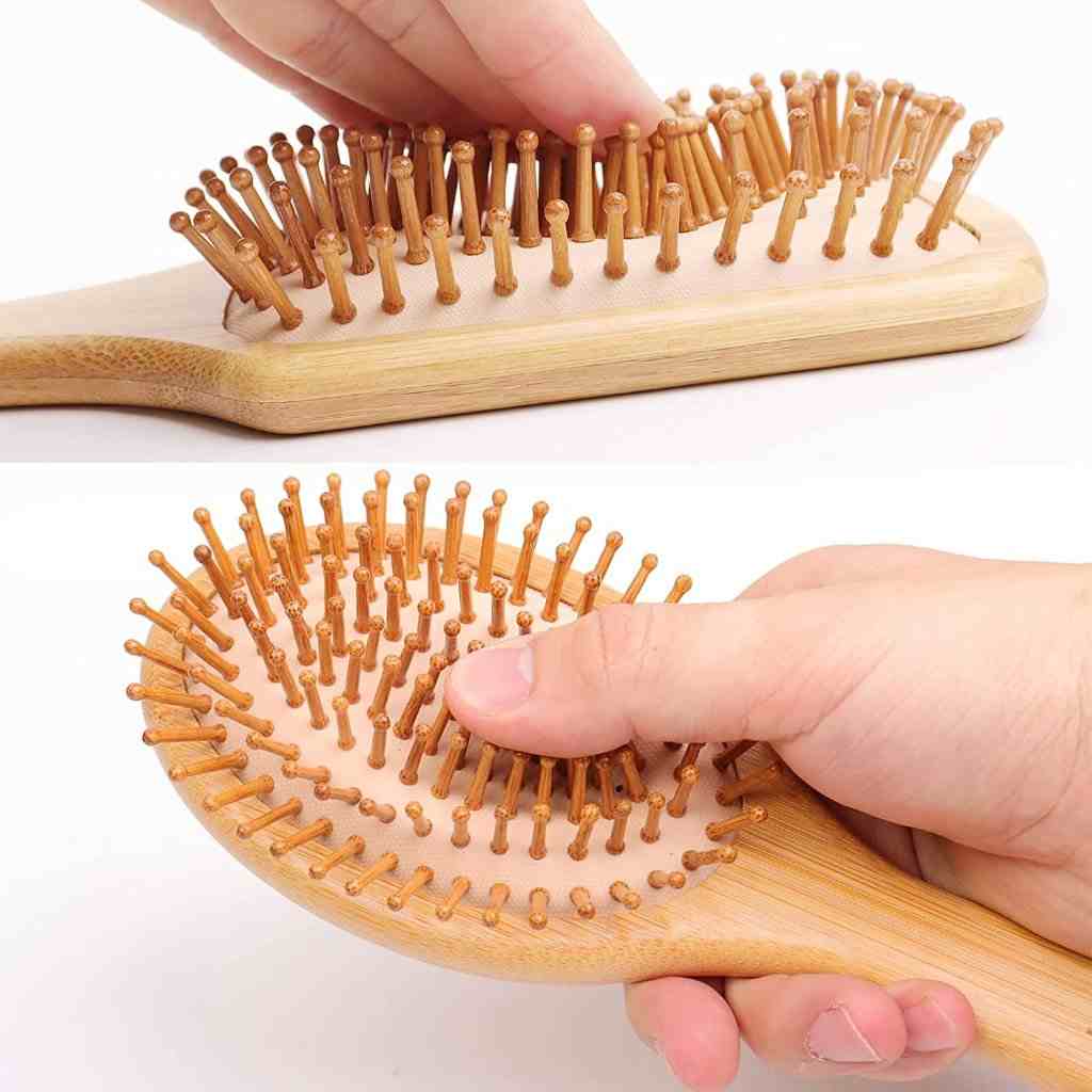 Close-up of a wooden hairbrush with flexible bristles being pressed, demonstrating its soft, cushioned surface.