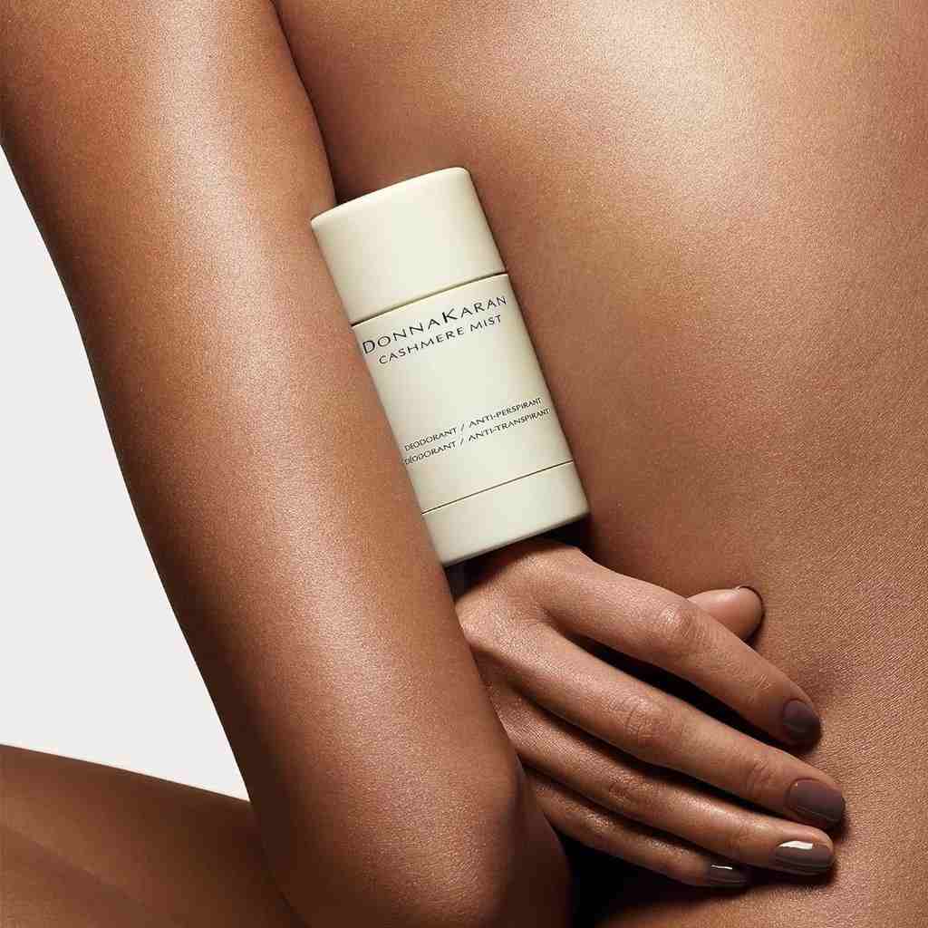 Close-up of a woman holding a Donna Karan Cashmere Mist deodorant stick against her bare skin, highlighting luxury and freshness.