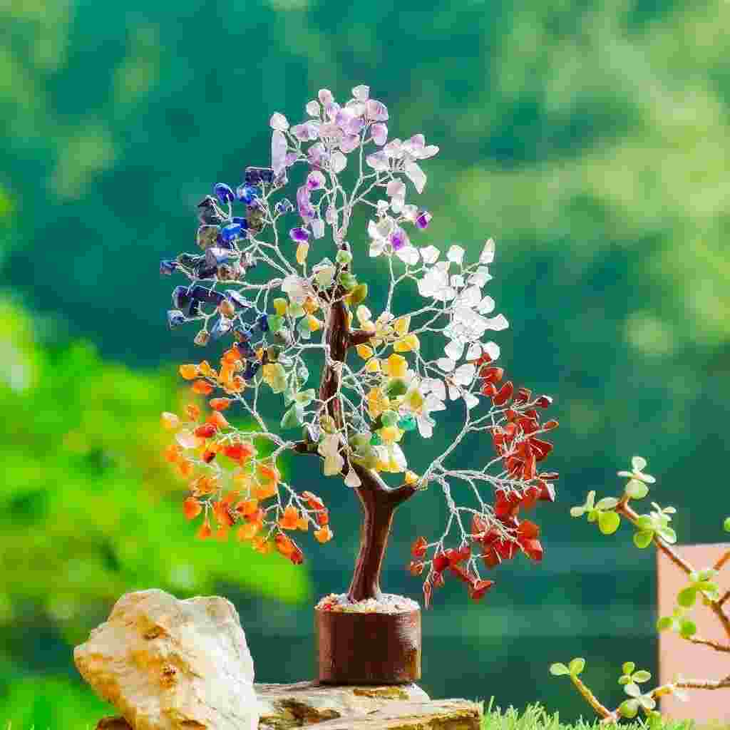 A colorful gemstone tree sculpture with branches adorned in various crystal stones, displayed outdoors against a green background.