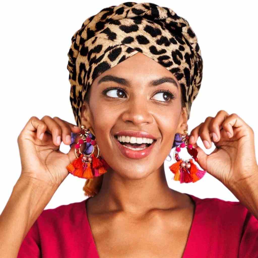 Leopard print turban and bright tassel earrings worn by a cheerful woman in a red dress, ideal for a vibrant and stylish ensemble.