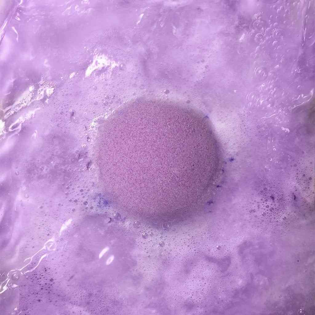 Close-up of a lavender bath bomb fizzing in water, producing soothing purple foam and a calming scent for a relaxing bath.