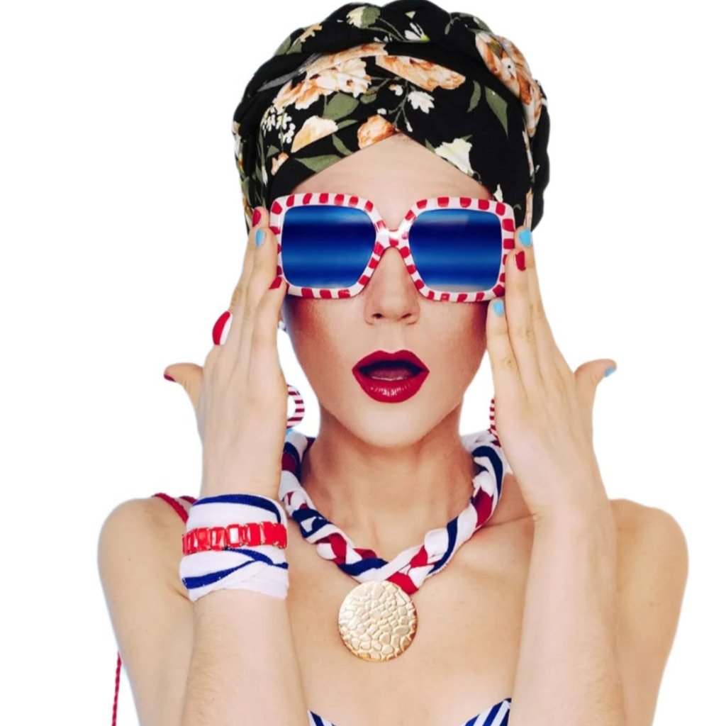 Chic woman in bold sunglasses, wearing a floral pre-tied turban and nautical-themed outfit, showcasing a surprised expression.