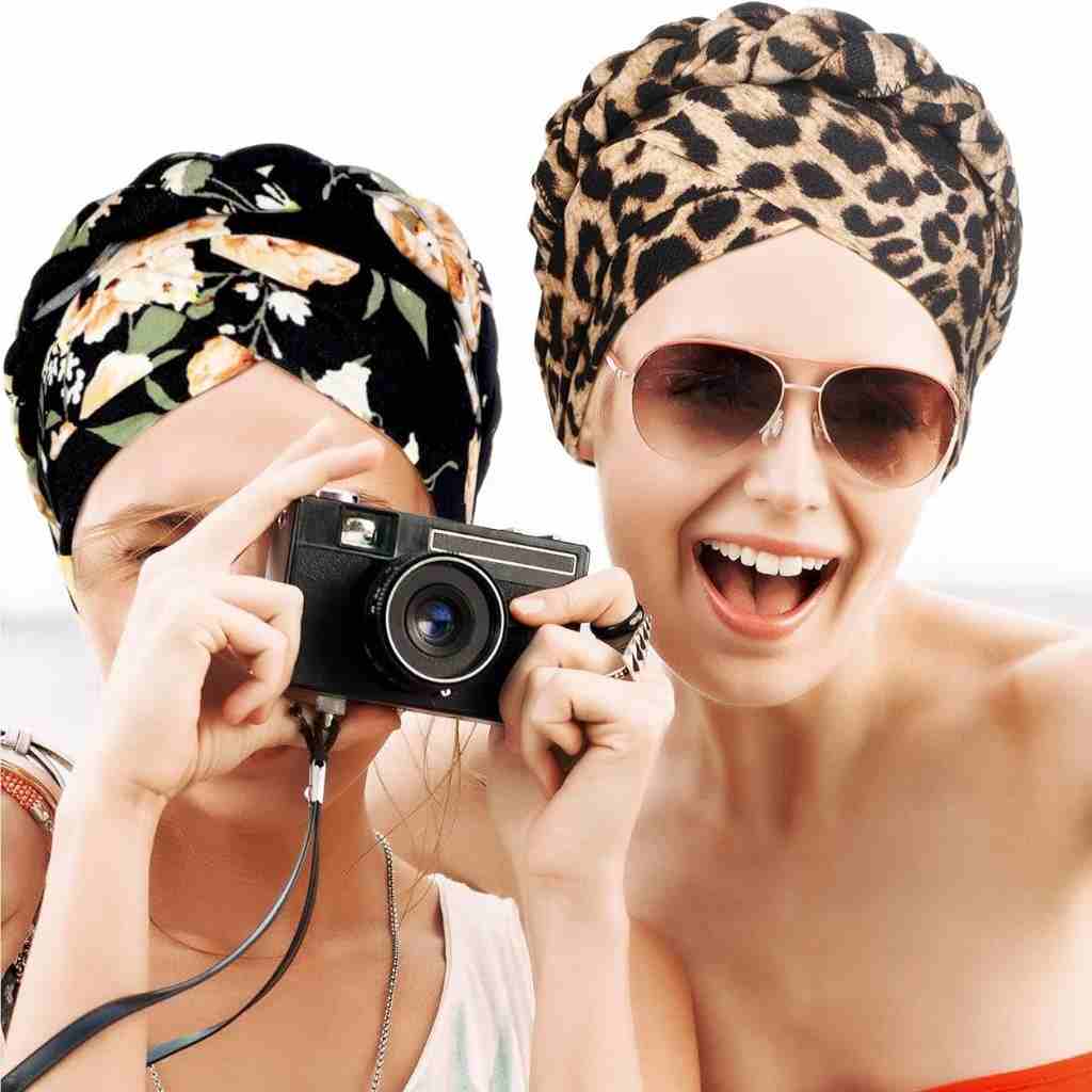 
Two women are enjoying a sunny day, sporting fashionable pre-tied turban head wraps in floral and leopard prints.