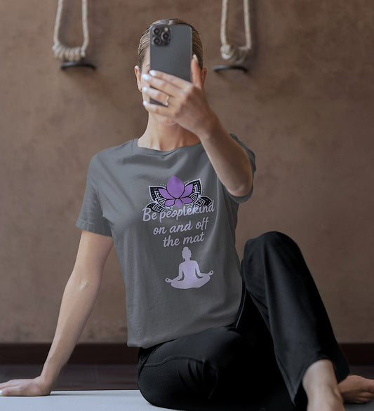 Woman wearing Asphalt Bella Canvas 3001 t-shirt with lotus and "Be peoplekind" quote, taking a selfie after yoga on mat.