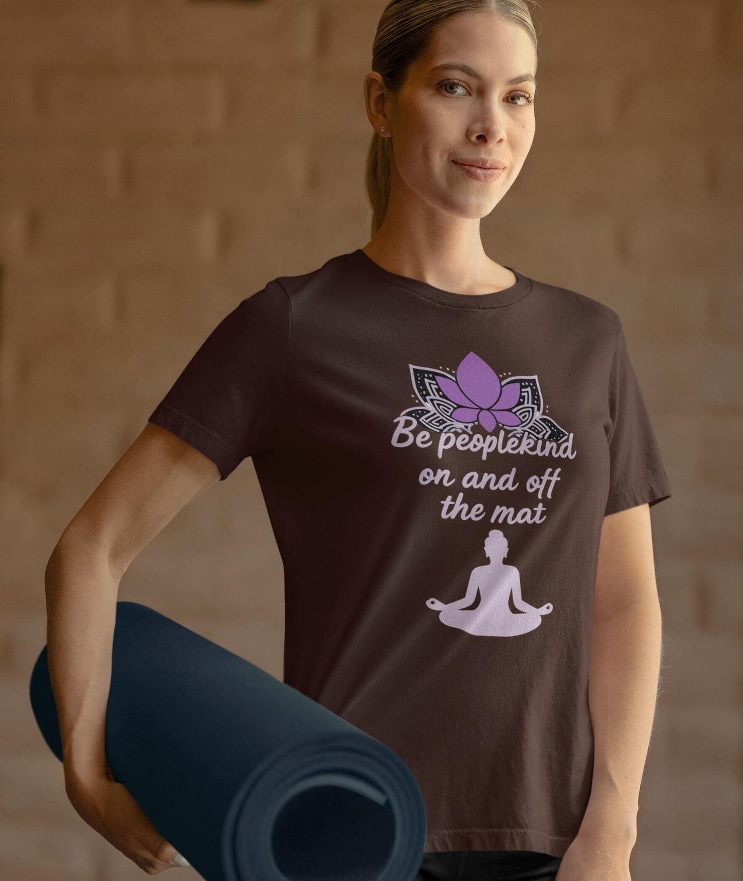 Woman in brown Be Peoplekind yoga shirt holding mat, promoting mindfulness, kindness, and spiritual lifestyle.