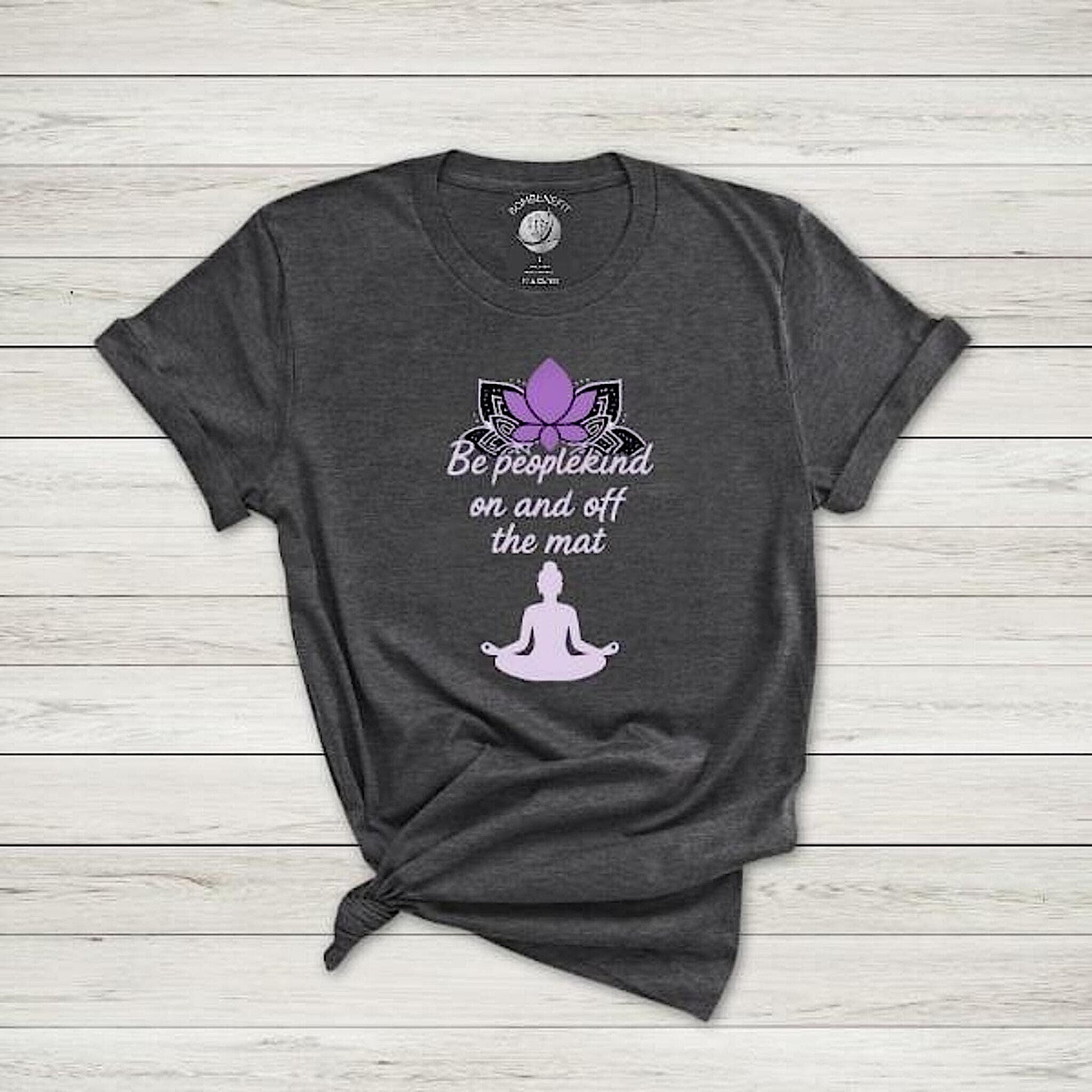 Dark Grey Heather Bella Canvas 3001 t-shirt with lotus and "Be peoplekind on and off the mat" quote, flat lay on wood.