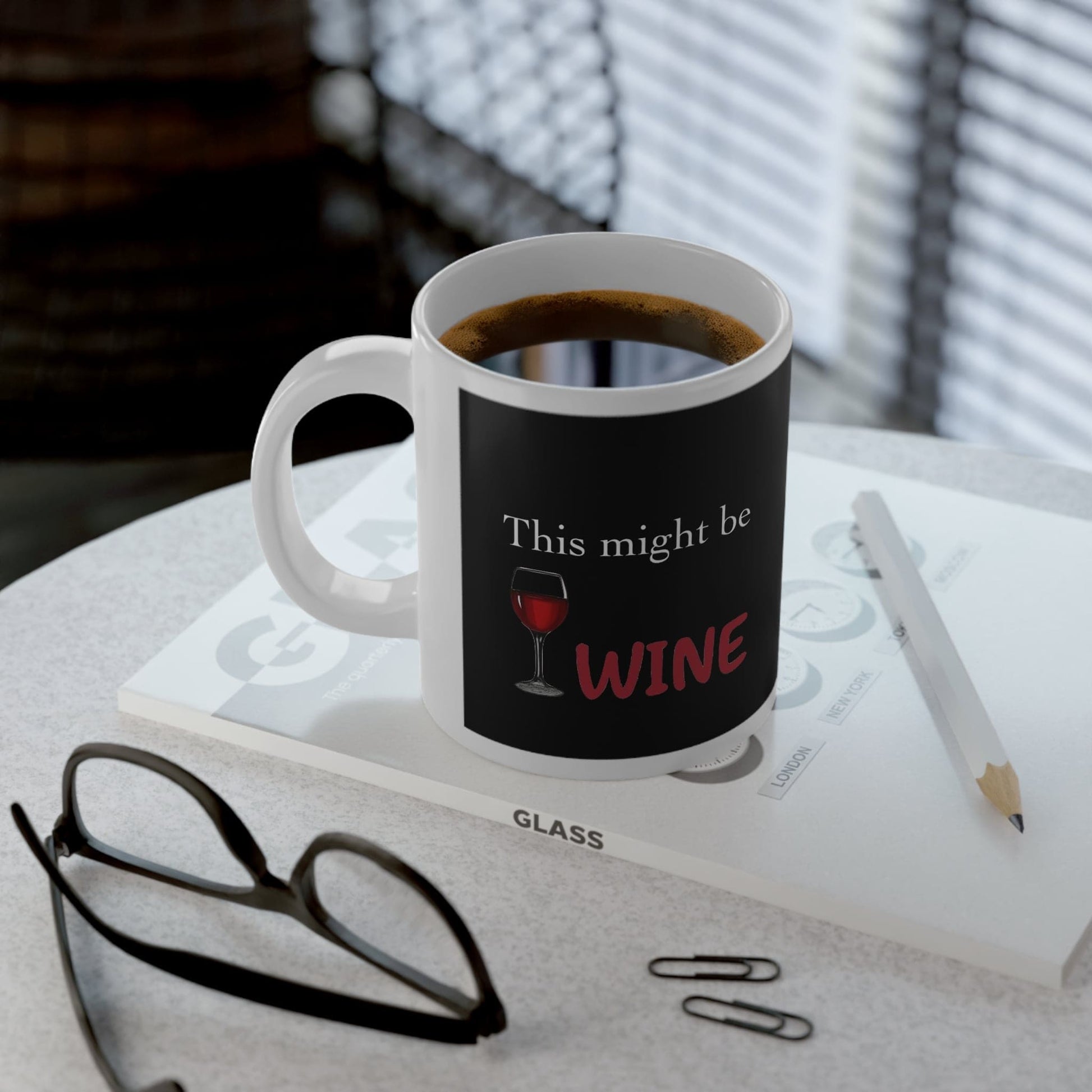 Funny coffee mug with "This might be wine" text on office desk with coffee, glasses, pencil, and paper clips