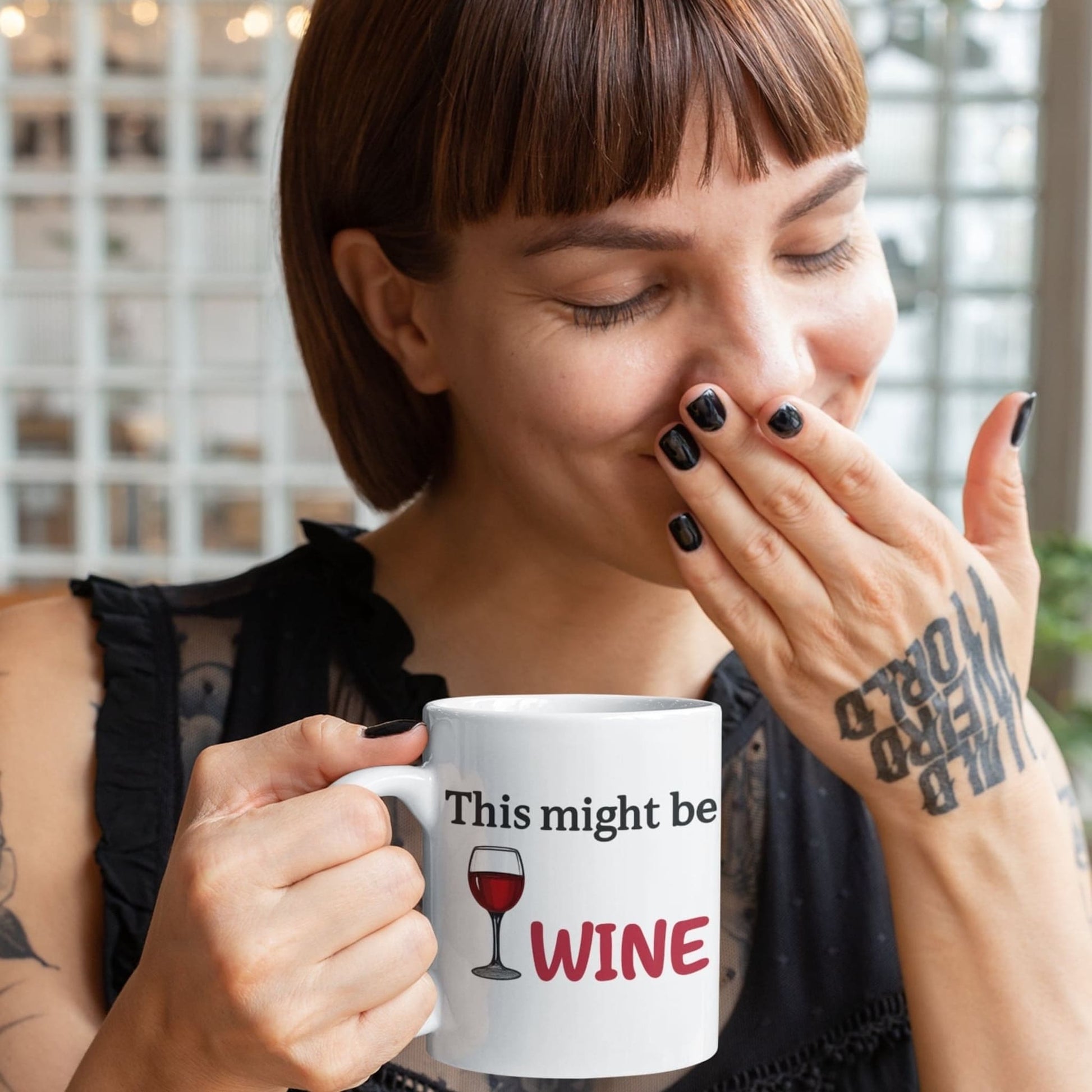 Woman smiling and holding a funny light grey mug that says "This might be WINE" with a red wine glass illustration