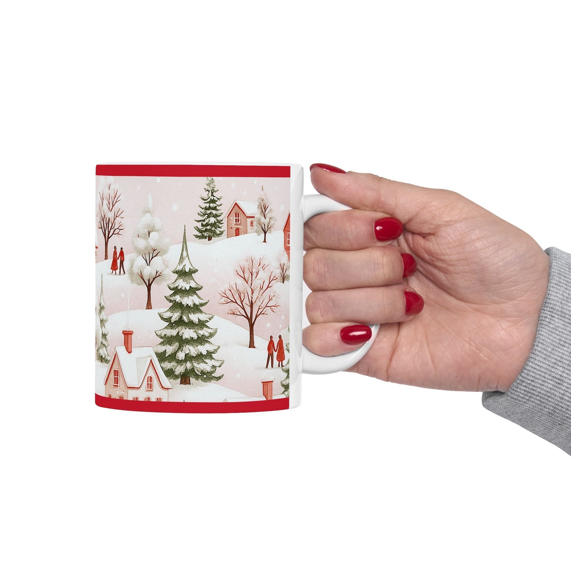 Hand holding white ceramic 11oz mug with red winter village scene, snowy trees, houses, and couples walking in a festive landscape.