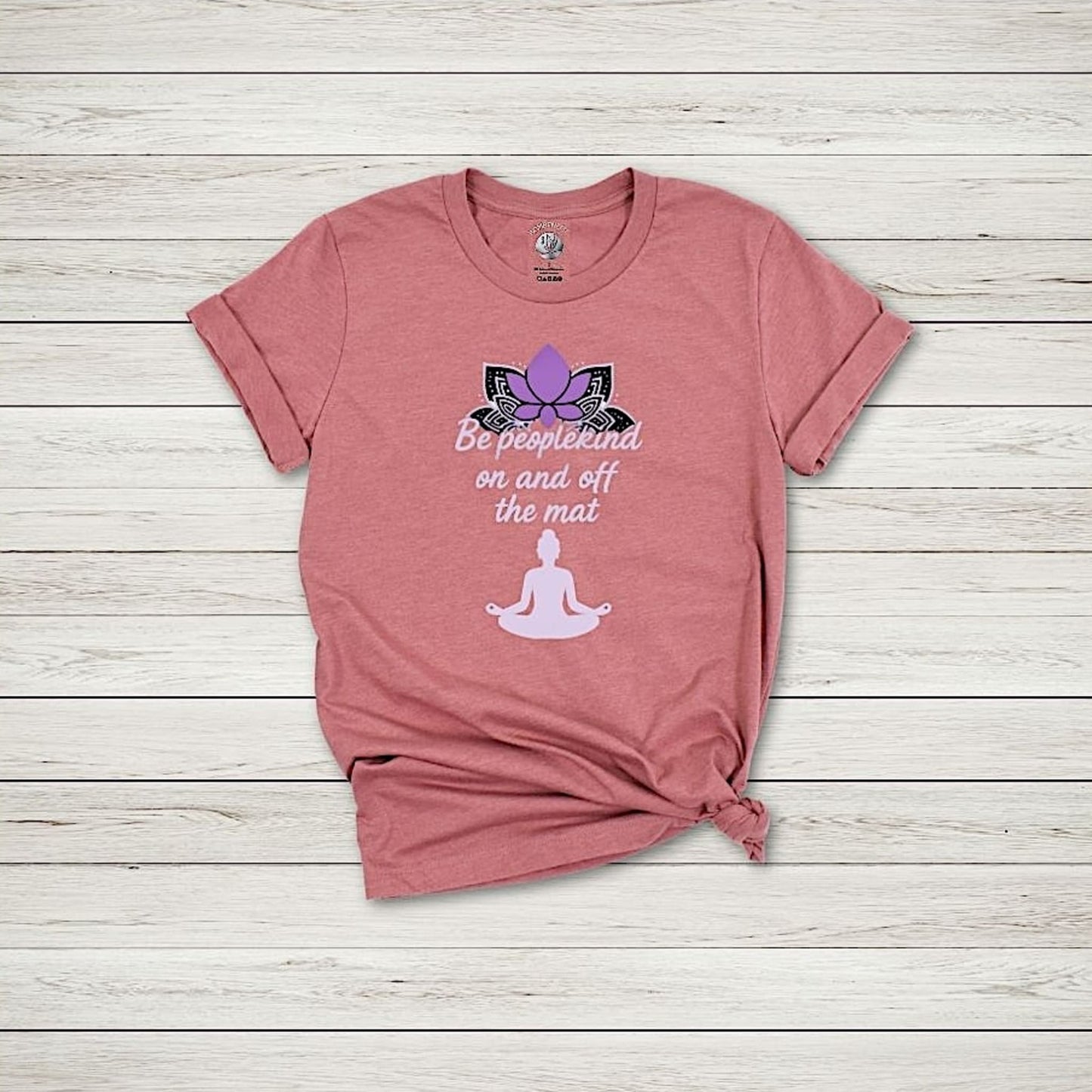 Heather mauve Be Peoplekind yoga t-shirt with lotus design and meditation quote styled flat on wood background.