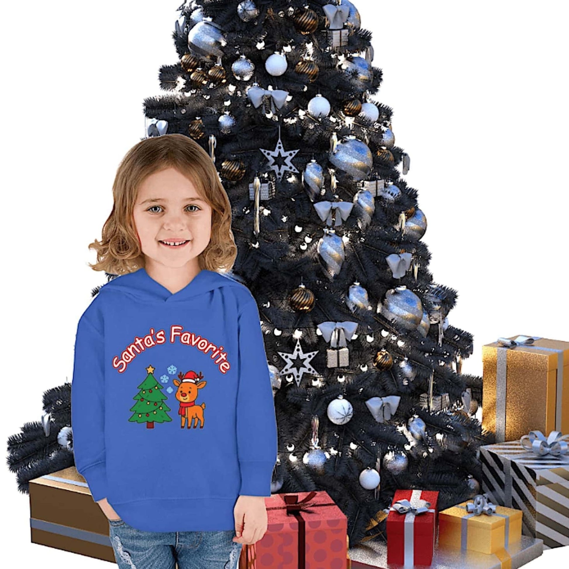 Smiling child wearing a blue Santa's Favorite reindeer Christmas hoodie standing in front of a decorated Christmas tree with gifts
