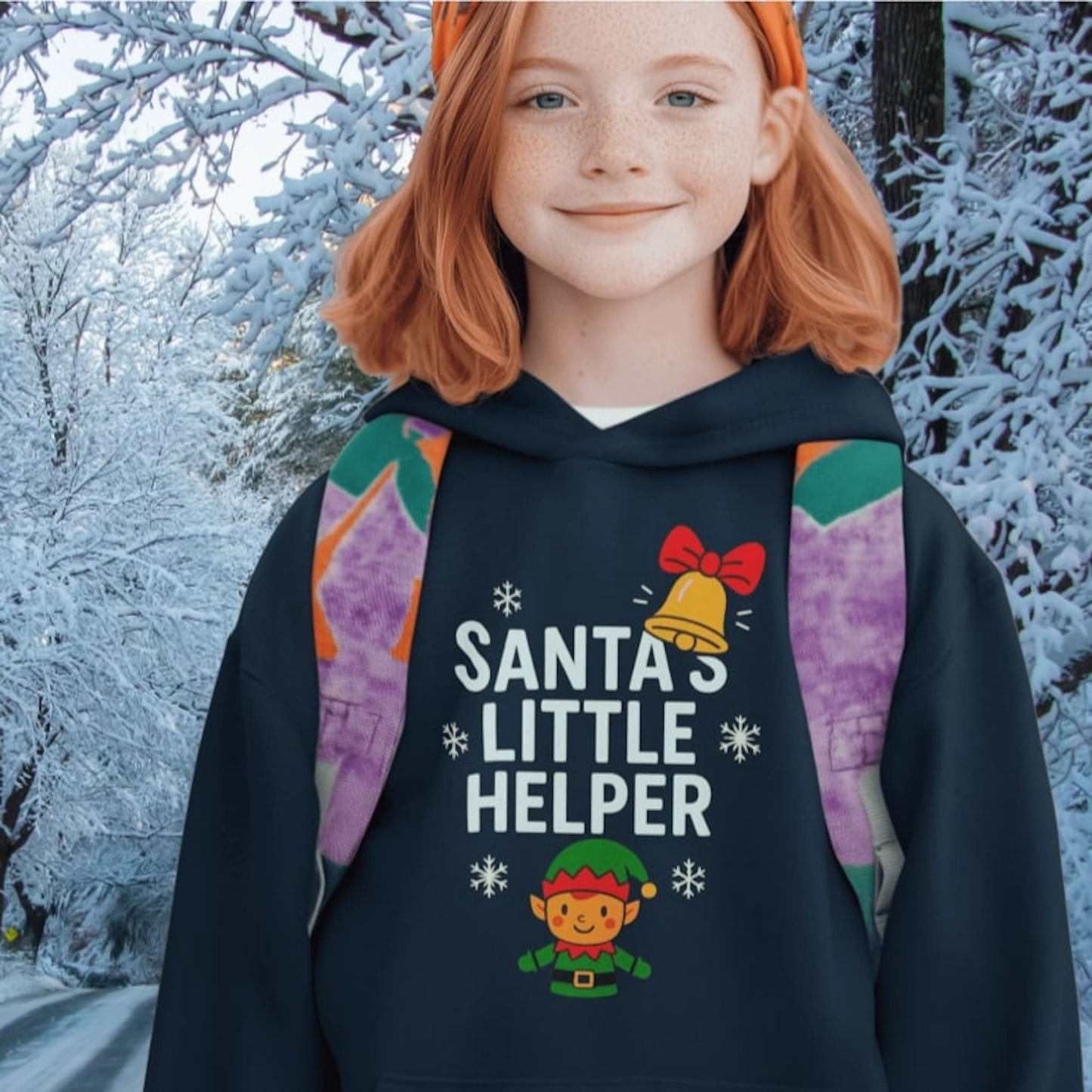 Girl wearing navy hoodie with Santa’s Little Helper design, featuring elf, bell, and snowflakes, festive Christmas clothing.