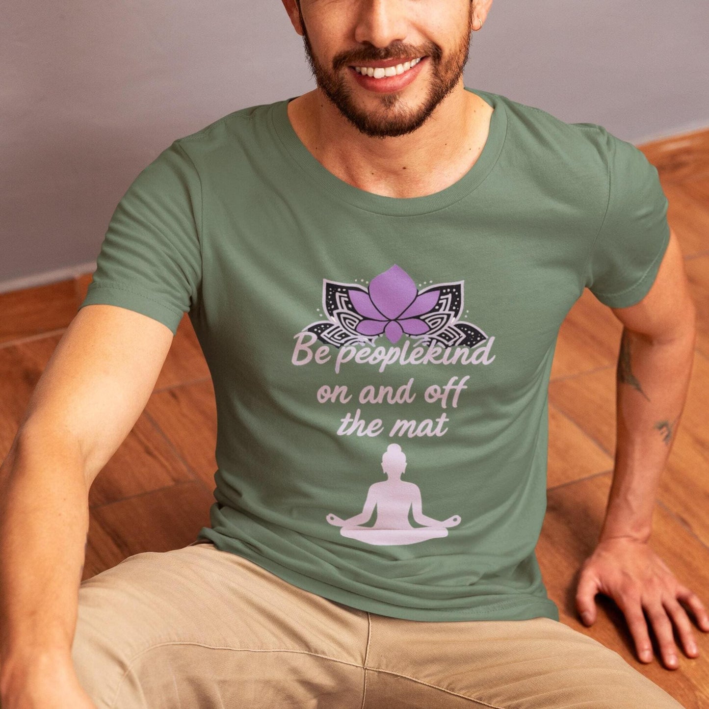 Man wearing military green yoga t-shirt with Be Peoplekind on and off the mat design sitting on wooden floor