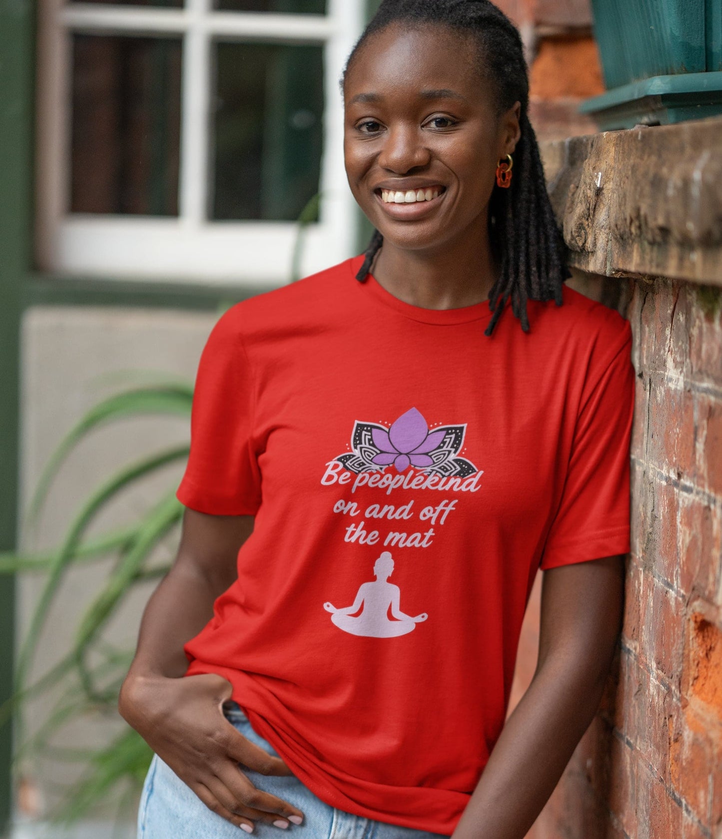 Smiling woman wearing red Be Peoplekind yoga shirt promoting mindfulness and kindness on and off the mat.