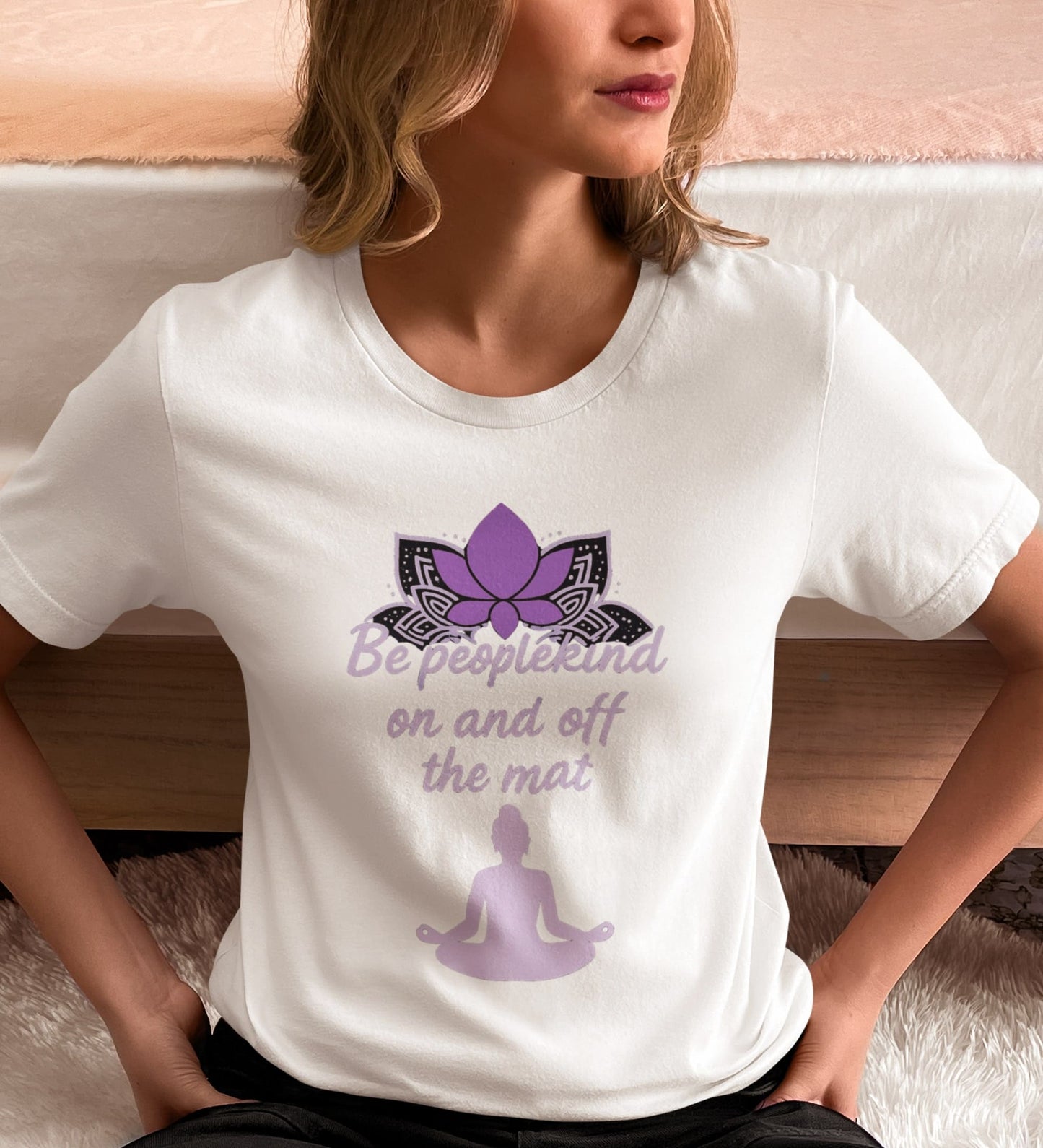 Woman wearing White Bella Canvas 3001 t-shirt with purple “Be peoplekind” yoga design, sitting near bed at home.